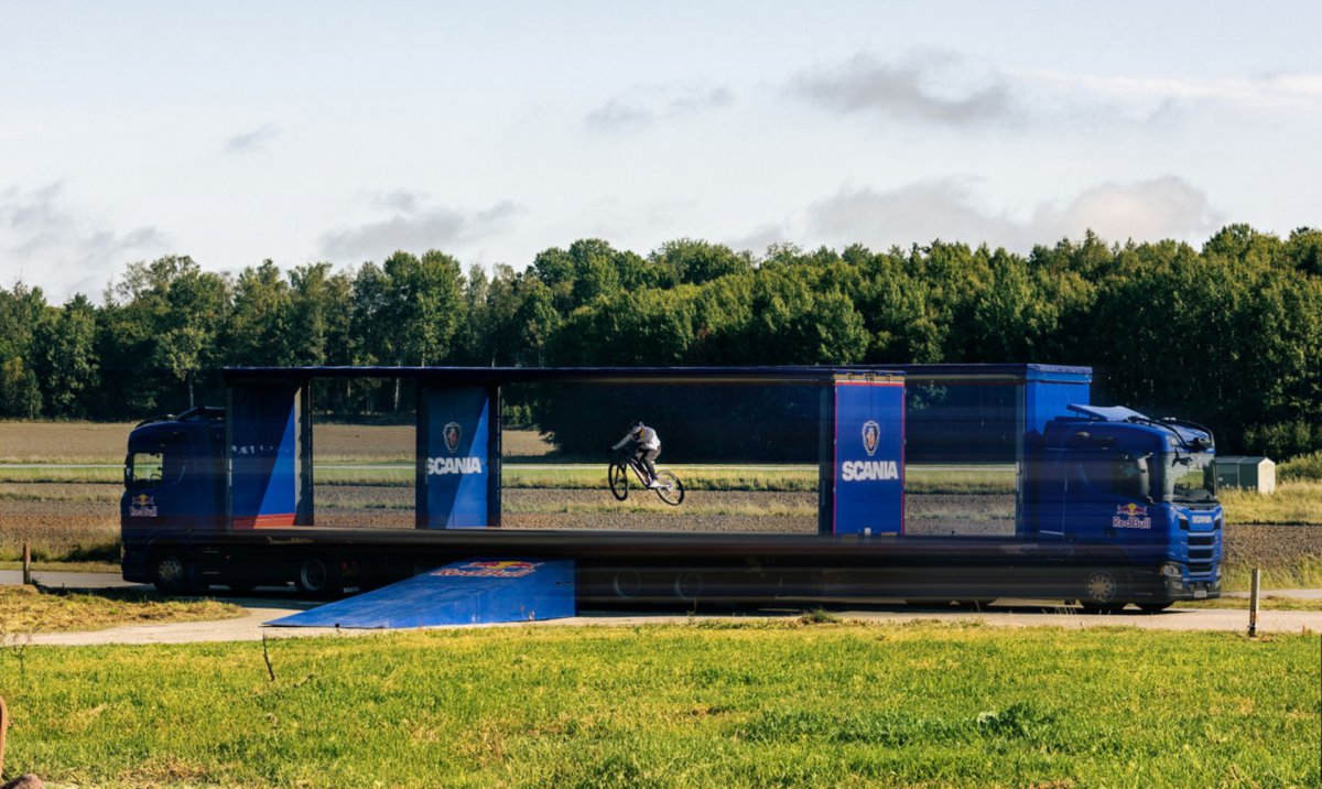 Red-Bull-Profi-Mountainbiker-springt-durch-zwei-fahrende-autonome-Scania-Lkw