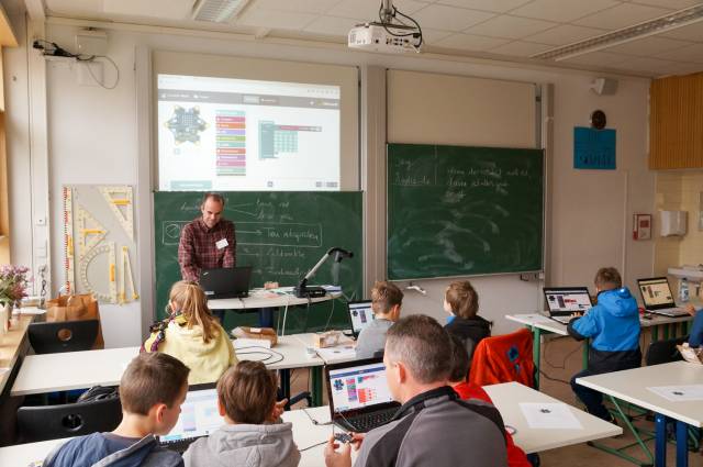 In einem Klassenraum sitzen Kinder mit Laptops