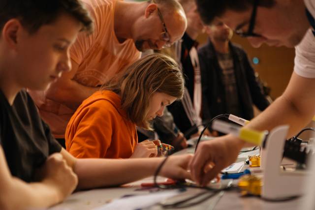 An einem Tisch in der Stadthalle Chemnitz löten während der Maker Faire Sachsen verschiedene Erwachsene und Kinder.