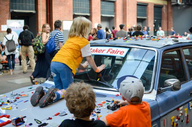 Ein Kind sitzt auf einem alten Auto, das mit Legokreationen geschmücktist.