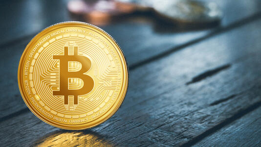 G&uuml;ldene M&uuml;nze mit Bitcoin-Logo steht auf einem Holztisch