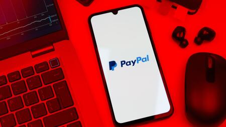Rotes Foto eines Schreibtischs, in der Mitte ein Smartphone mit dem payPal-Logo