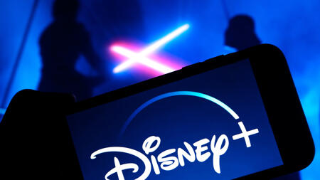 Disney+-Schriftzug auf einem Bildschirm; dahinter kreuzen zwei Schattengestalten Lichtschwerter