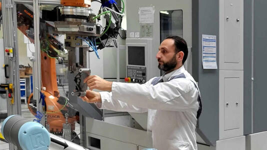 Mann in Kittel arbeitet mit einem Roboter.