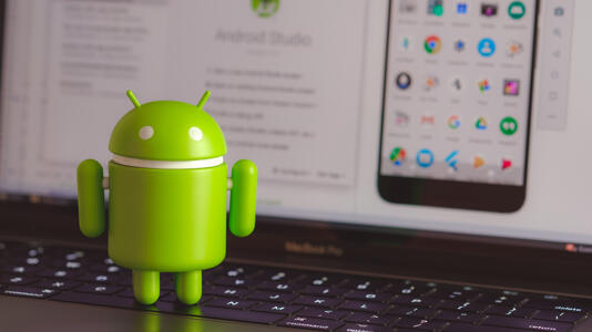 Android-Maskottchen vor einem Bildschirm mit Android Studio