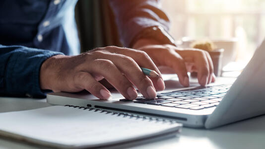 Eine Person macht eine Steuererklärung am Laptop und rechnet mit einem Taschenrechner nach
