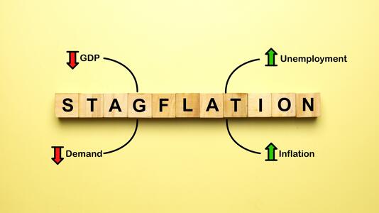 Holzwürfel mit dem Wort STAGFLATION und Pfeile, die sinkende BIP/Nachfrage und steigende Arbeitslosigkeit/Inflation anzeigen.