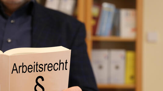 Ein Mann hält ein Buch mit der Aufschrift "Arbeitsrecht" und einem Paragraphenzeichen.