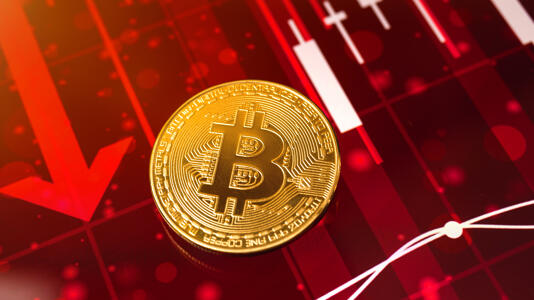 Eine Bitcoin-Münze, dahinter rote Pfeile, die nach unten zeigen