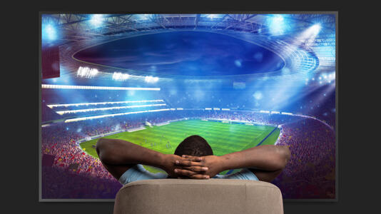 Mann blickt auf Fernseher, auf dem Fußball läuft.
