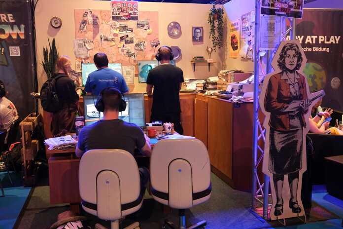 Menschen sitzen an Computern in einem Ausstellungsstand mit Karten und Postern an der Wand.