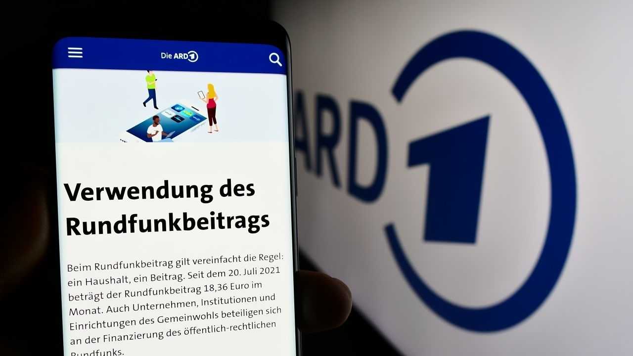 Person hält Smartphone mit Web-Seite des öffentlich-rechtlichen Rundfunks ARD vor Logo.