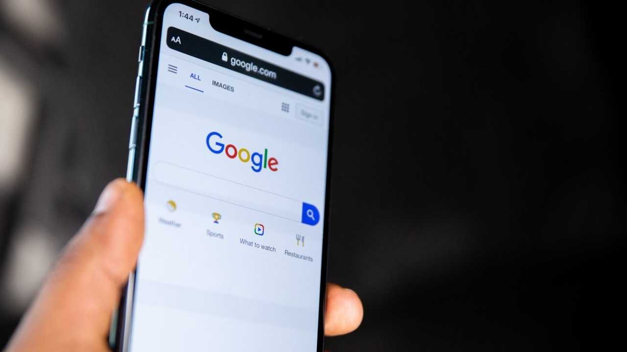 Smartphone mit Google auf dem Bildschirm, vor dunklem Hintergrund von einer Hand hoch gehalten