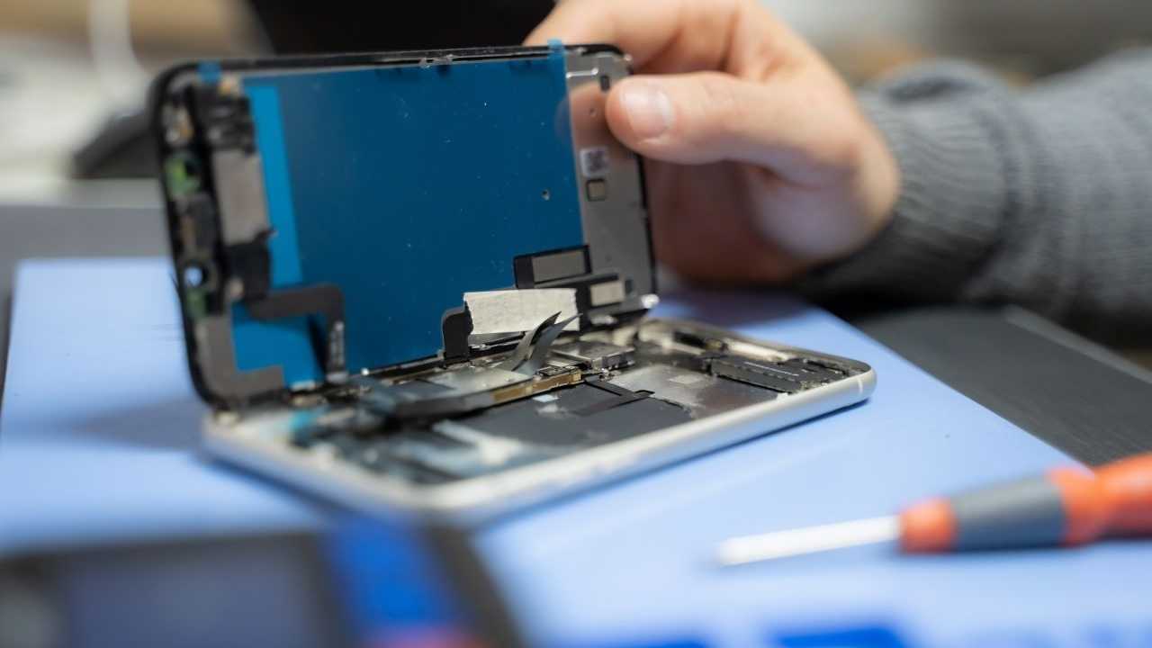 Geöffnetes Smartphone auf einem Tisch, daneben liegt ein Schraubenzieher. Zu sehen ist auch die Hand eines Reparateurs.