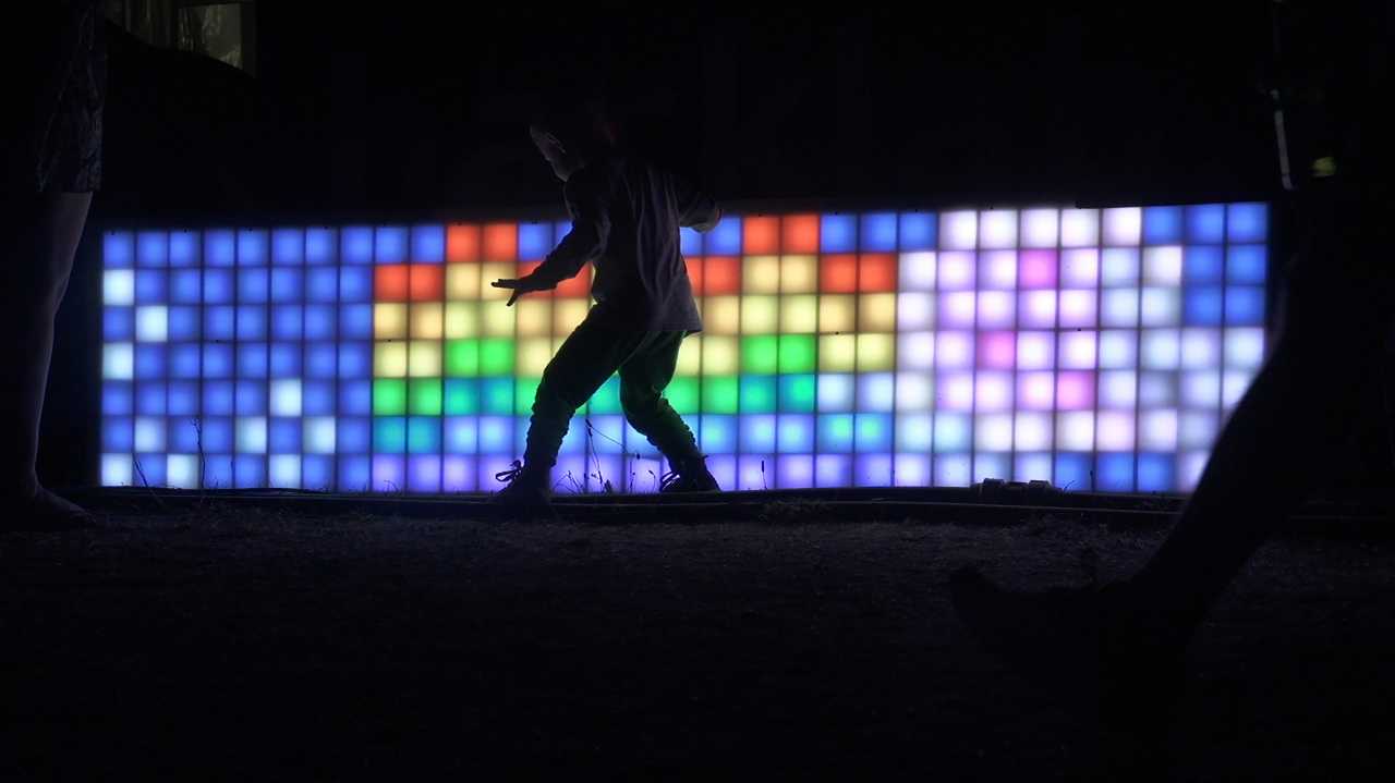 Schatten eines Kindes in der Nacht, vor bunter LED-Wand mit Nyan Cat.