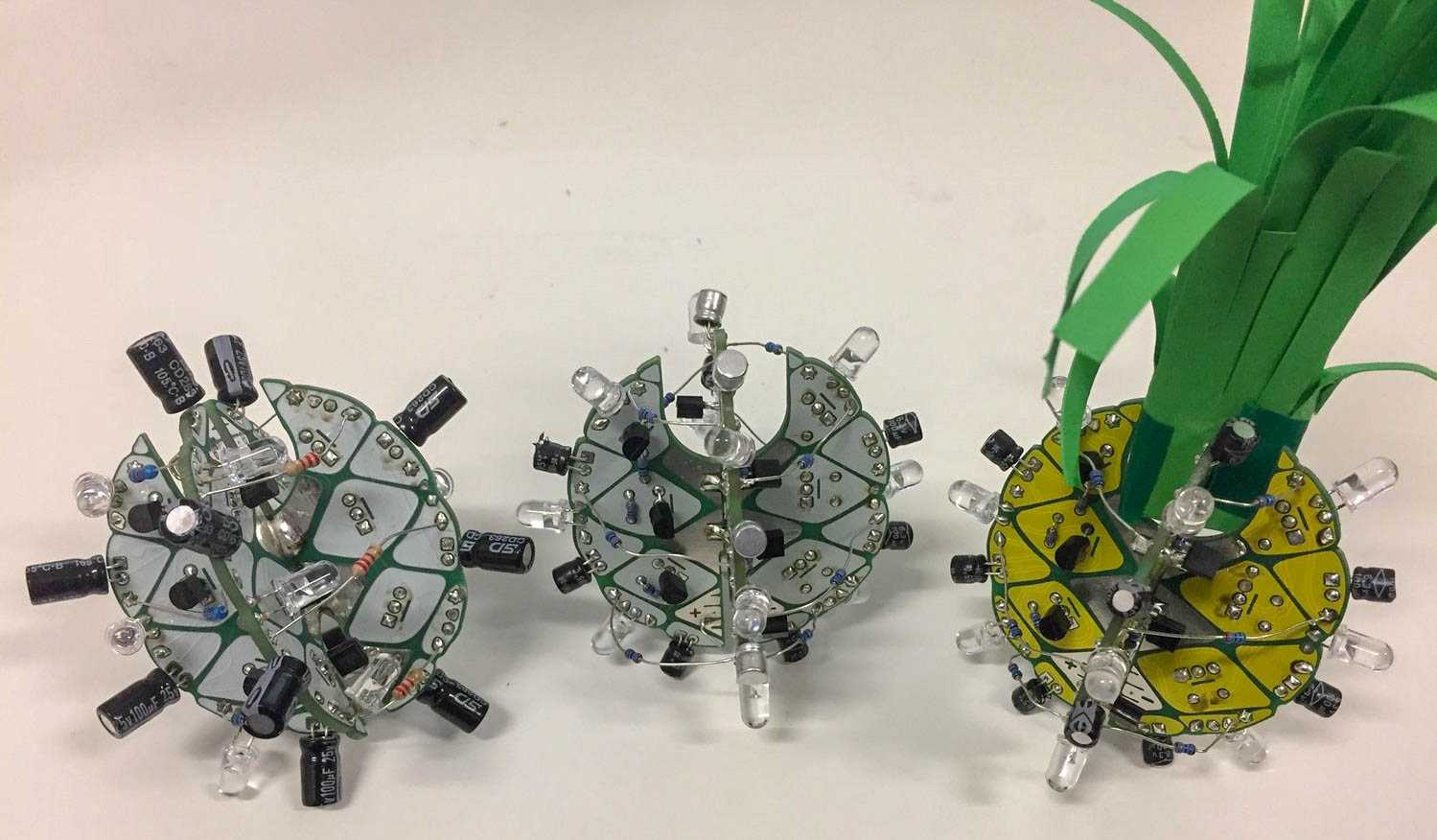 Drei Projekte aus zwei verschränkten Boards und aufgelöteten Komponenten, eines davon mit gelbem PCB und aufgestecktem Grün - wie eine Ananas.
