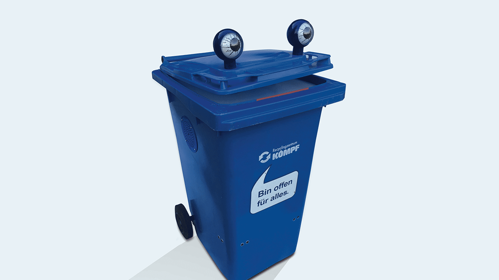 Blaue Mülltonne mit Stielaugen und einer aufgedruckten Sprechblase "Bin offen für alles." unter dem Markenlogo "Recyclingzentrum Kömpf".