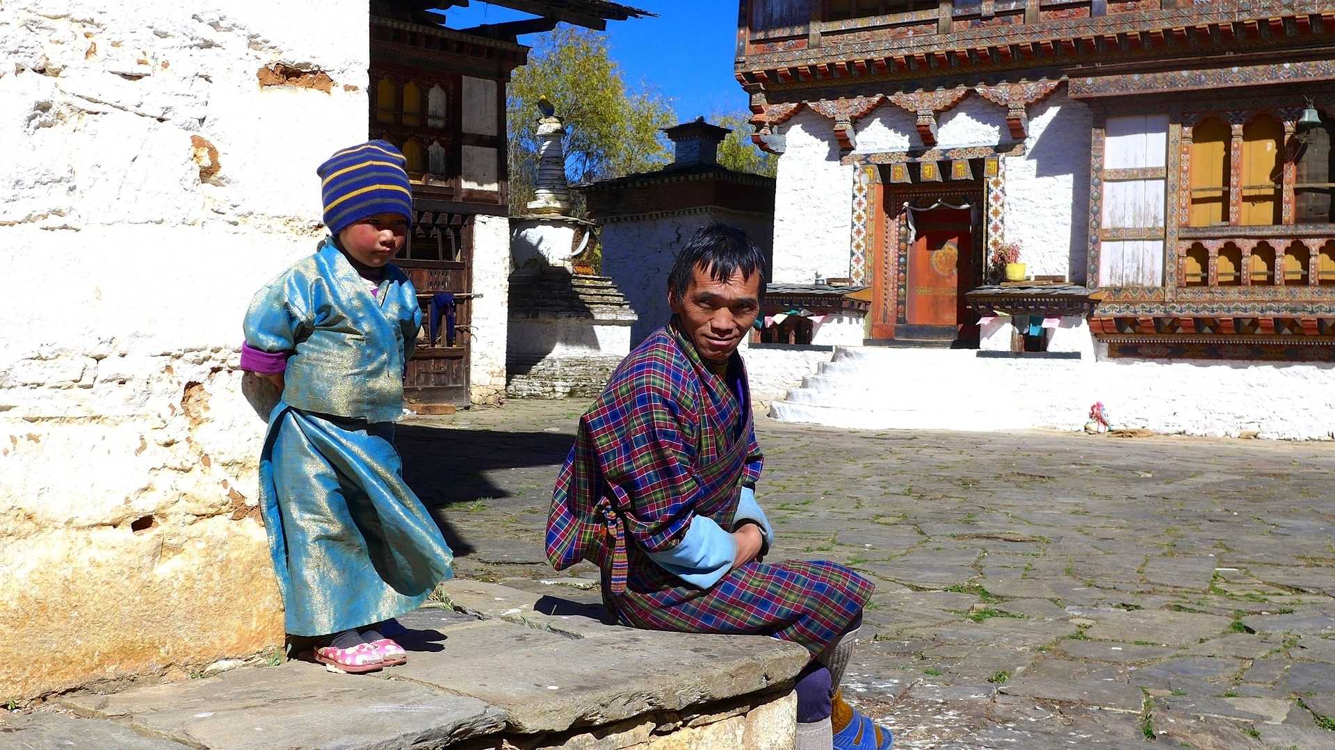 Vater und Kind in Bhutan vor ärmlichem Haus als Symbol für bescheidenen Lebensstil