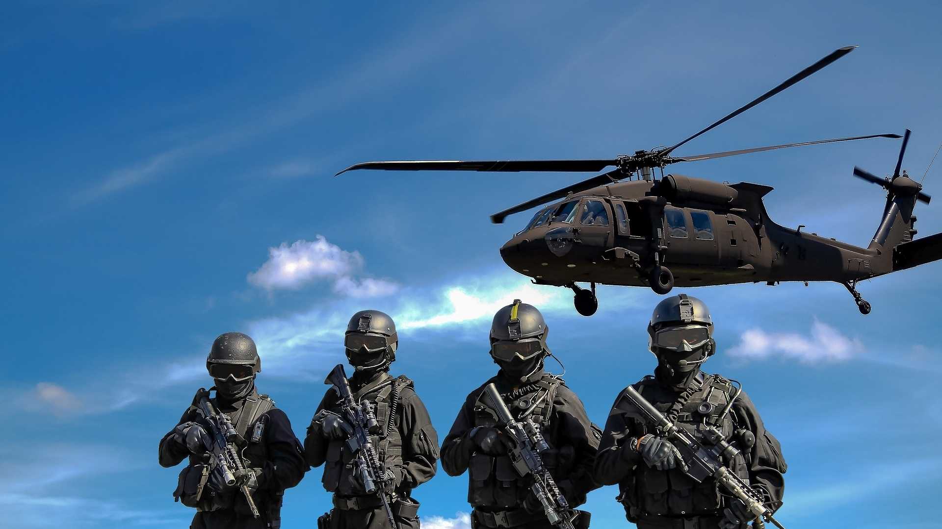 Bewaffnete Soldaten mit startendem Hubschrauber im Hintergrund