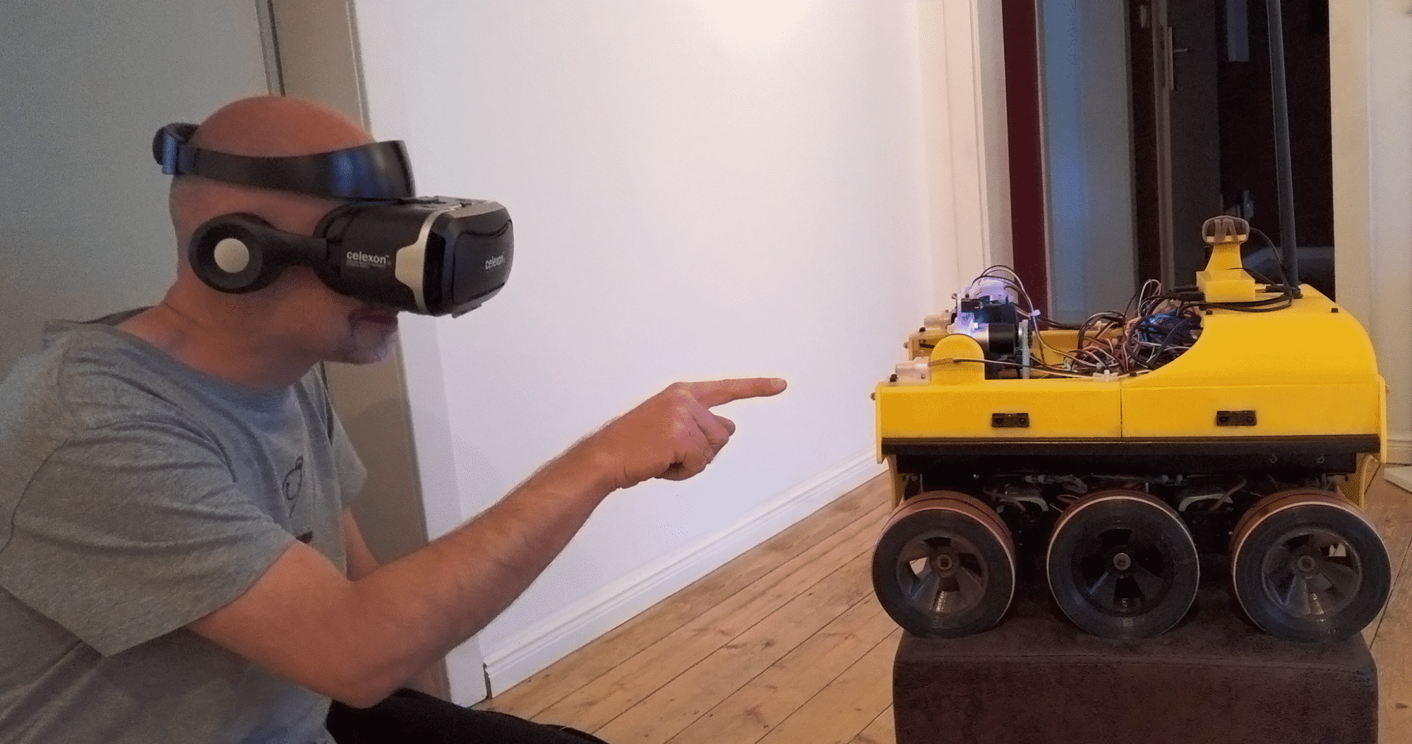 Ein Mann mit VR-Brille zeigt auf einen gelb-schwarzen Roboter