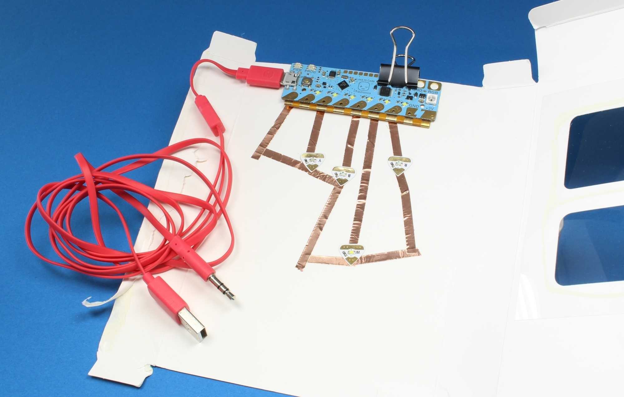 Auf einem weißen Papier ist ein blauer Mikrocontroller festgeklippt. An ihm hängt ein rotes Kabel.