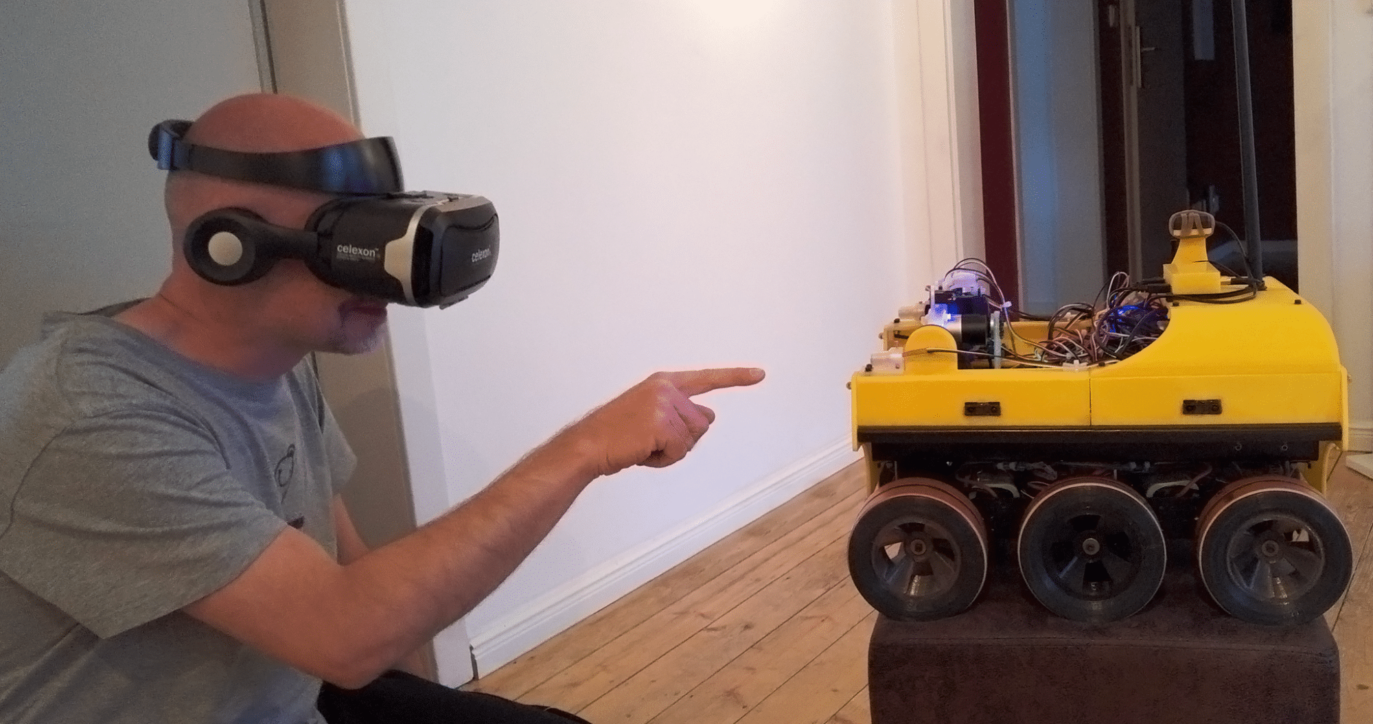 Ein Mann mit VR-Brille zeigt auf einen gelb-schwarzen Roboter