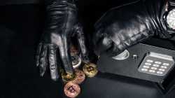 Geöffneter Tresor. 2 Hände mit Lederhandschuhen greifen nach Münzen mit Kryptowährungslogos