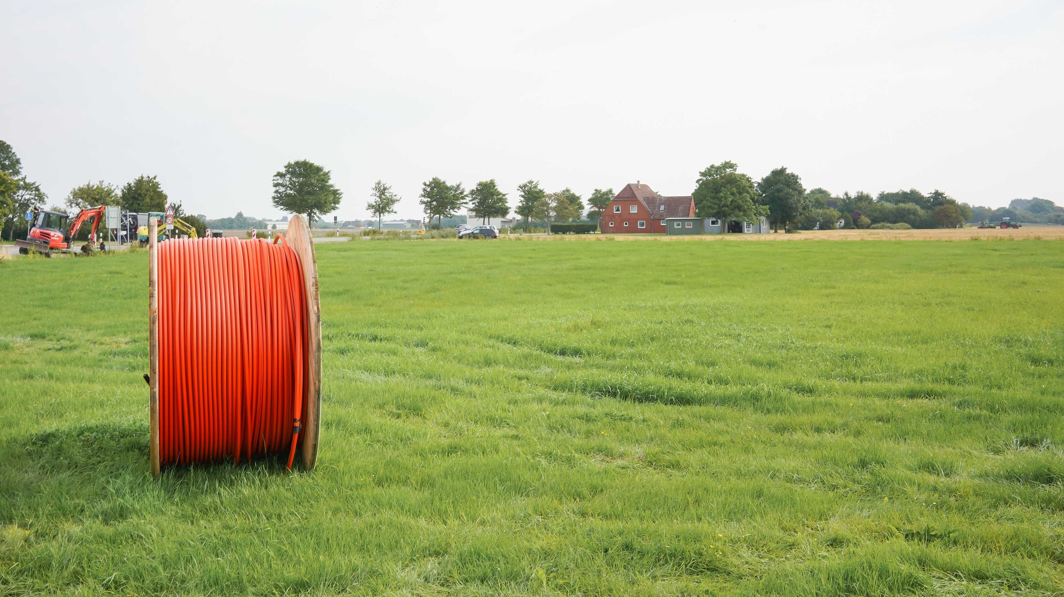 Eine große Kabeltrommel mit orangefarbenem Kabel steht auf einer günen Wiese
