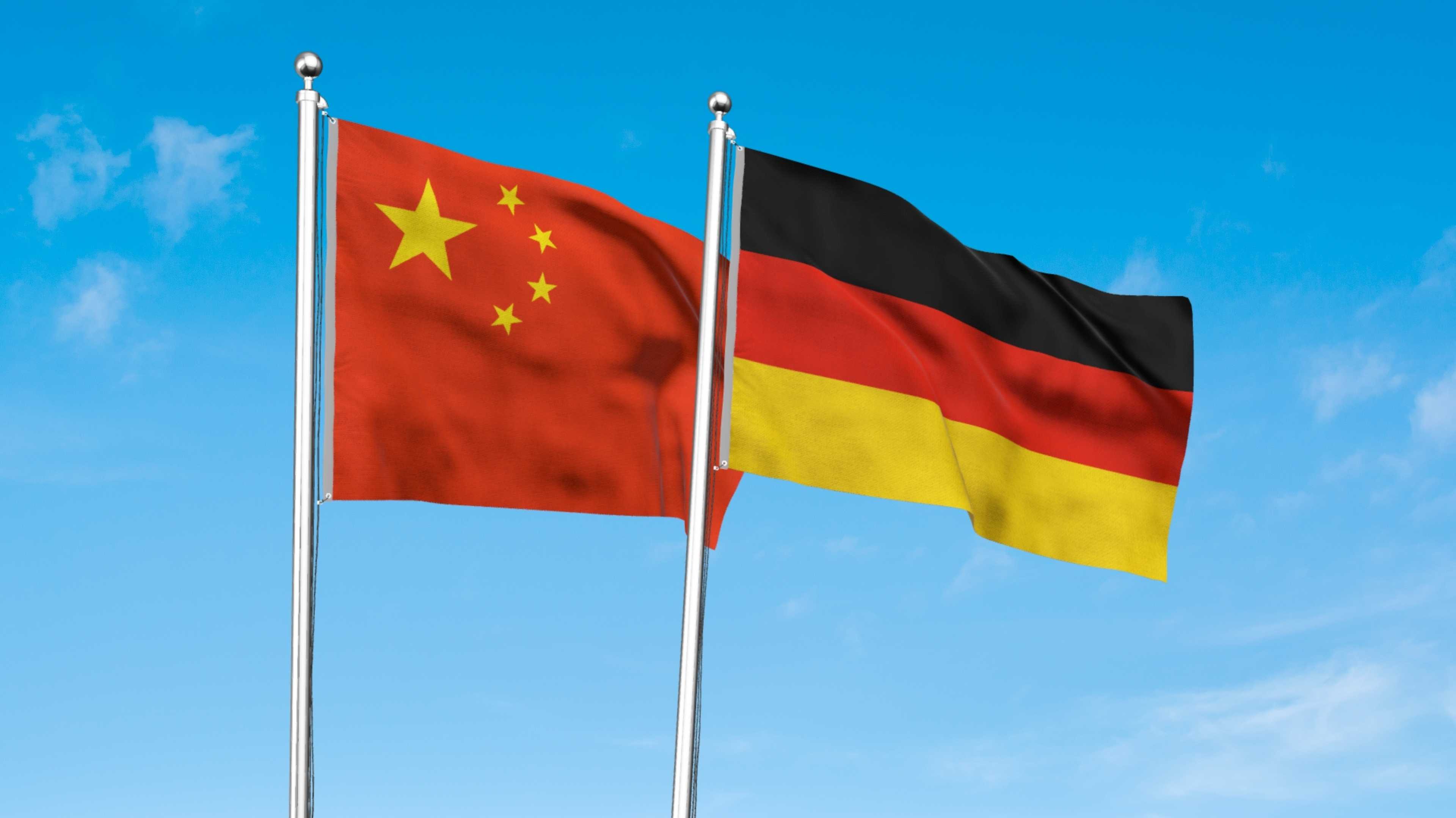 Eine chinesische und eine deutsche Fahne wehen vor blauem Himmel