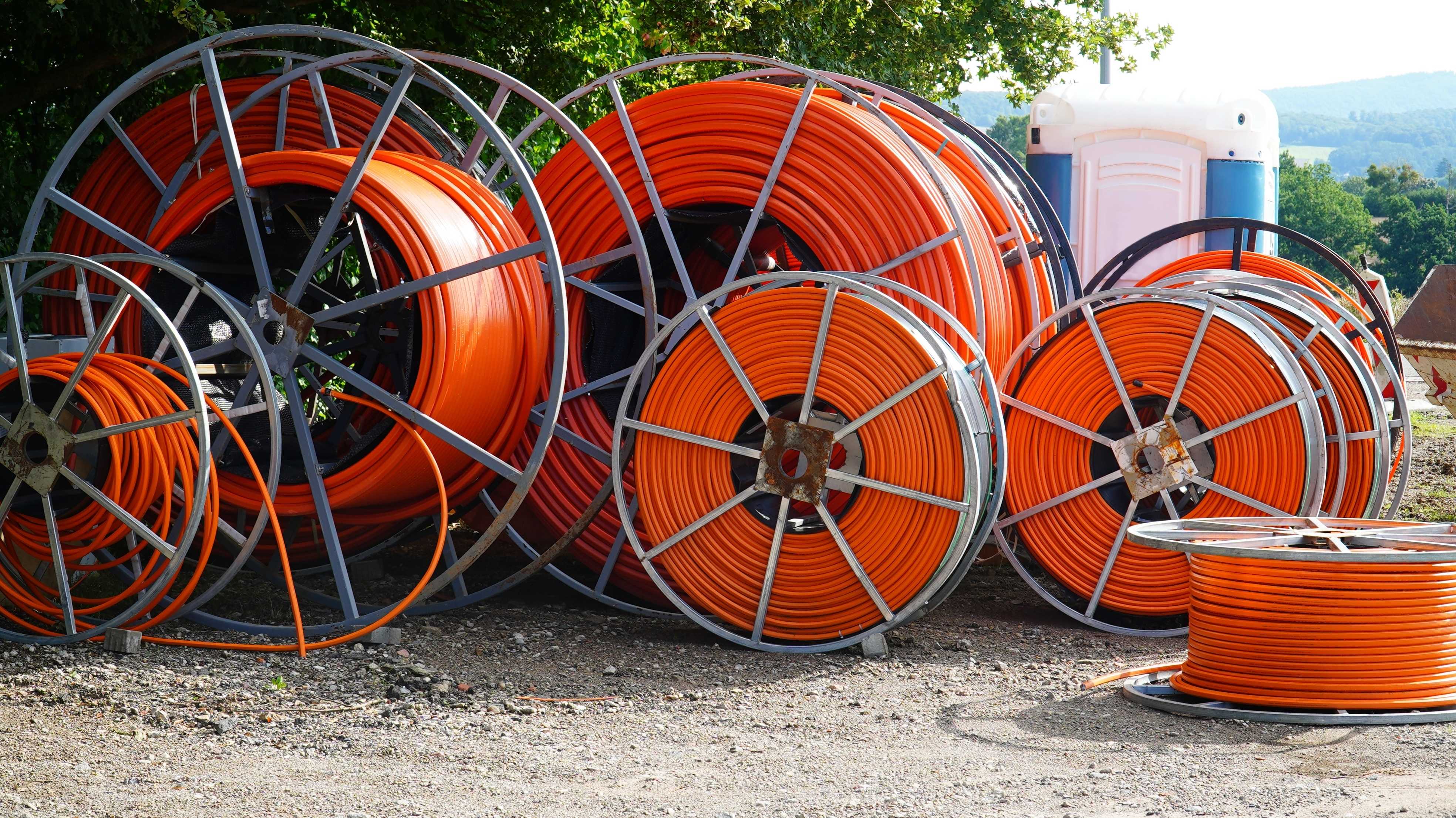 Große Rollen mit orangefarbenem Glasfaserkabel zur Verlegung im Boden an einer Baustelle in Beber, Niedersachsen.