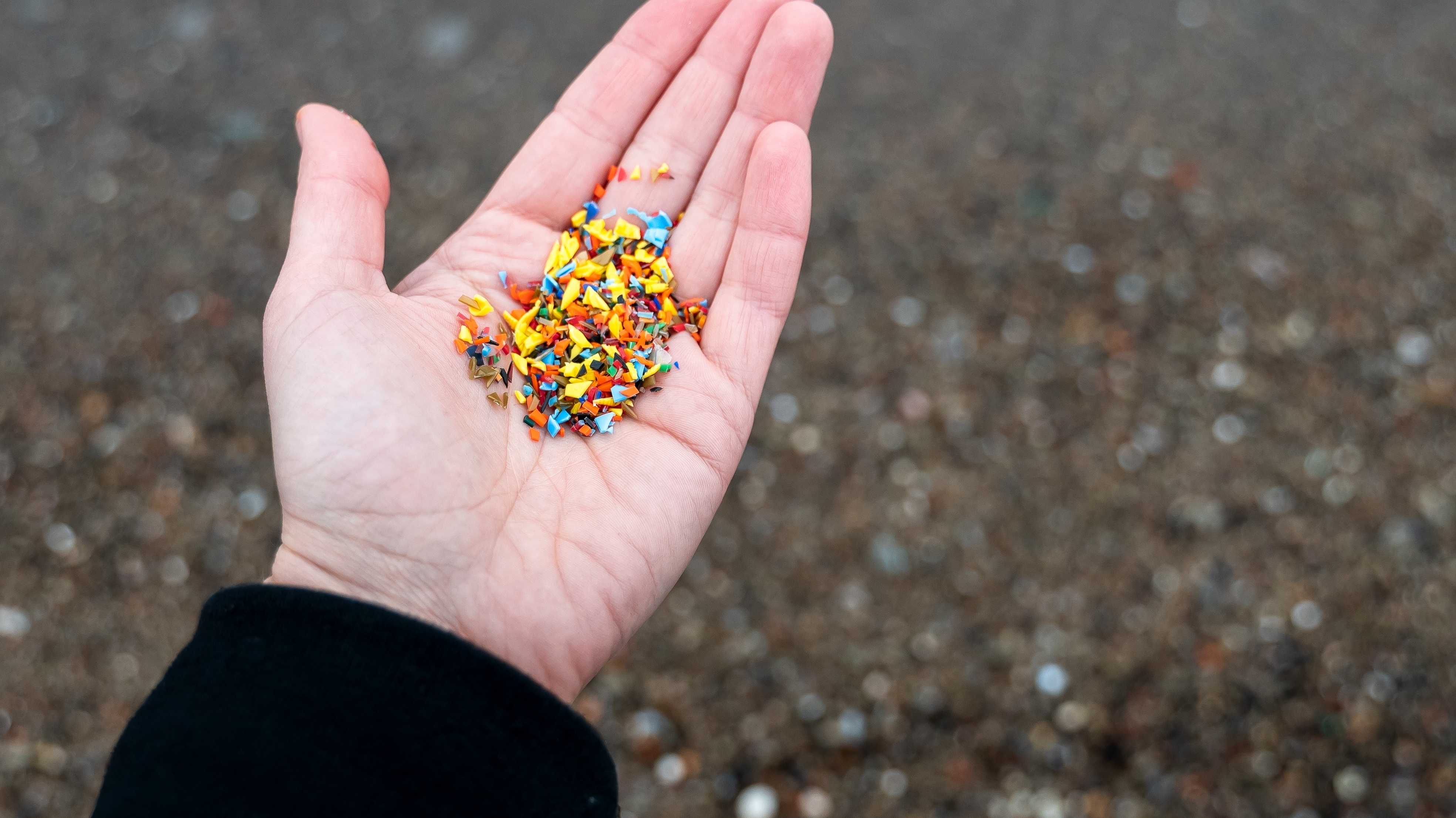 Offene Handfläche gefüllt mit winzigen Mikroplastikpartikeln auf unscharfem Sandstrand