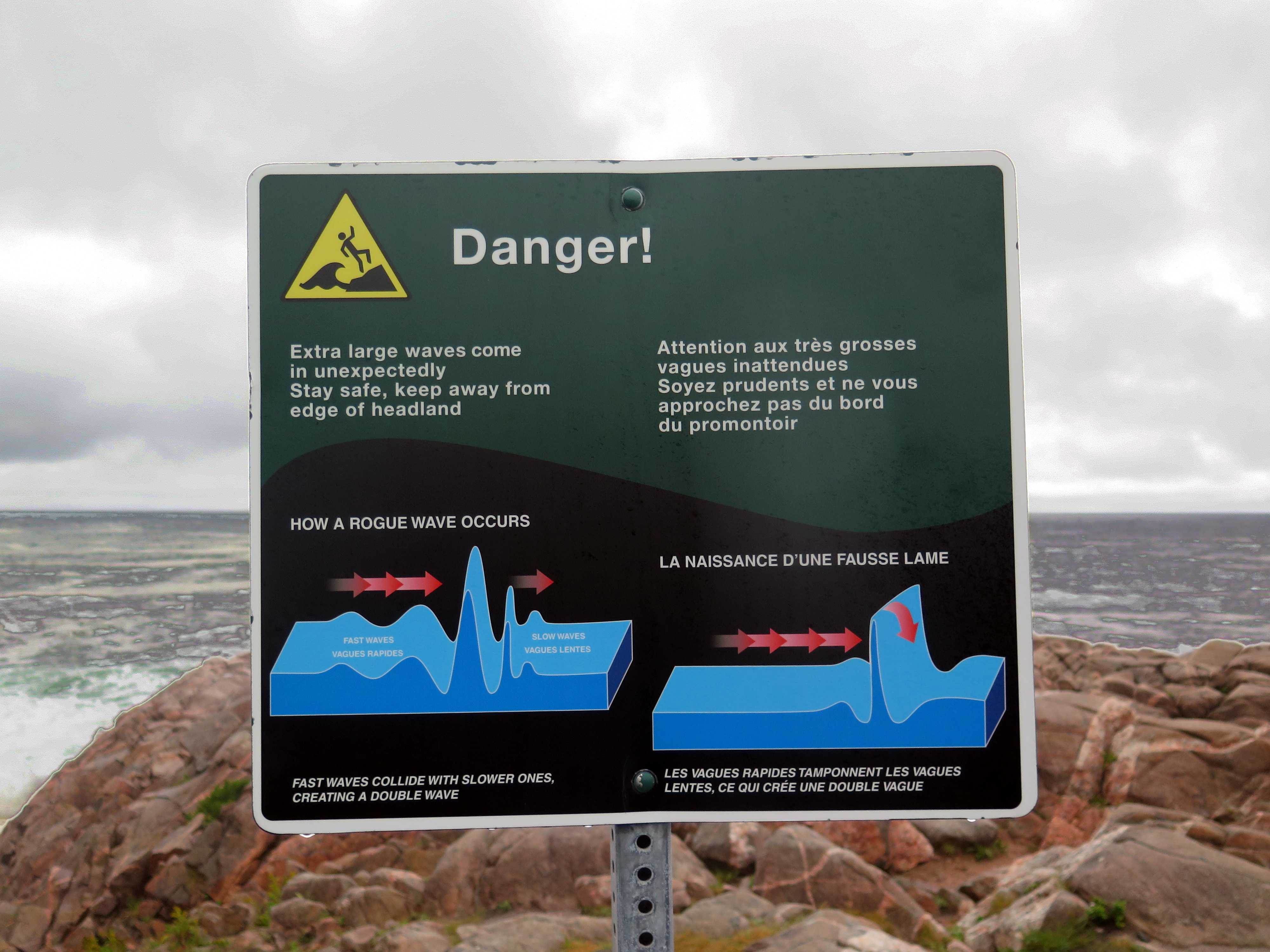 Warnschild &quot;Danger!&quot; in Englisch und Französisch, das vor Monsterwellen warnt und erklärt, wie sie entstehen