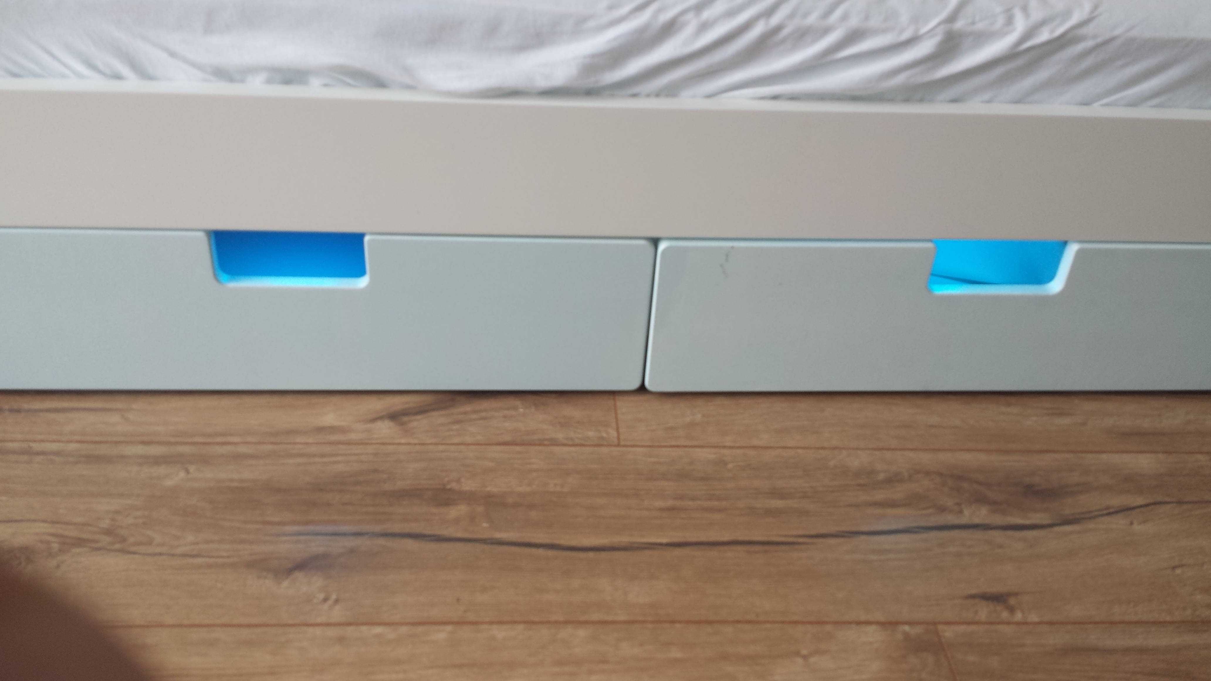 Aus zwei weißen Schubladen unter einem IKEA-Babybett leuchtet es türkis
