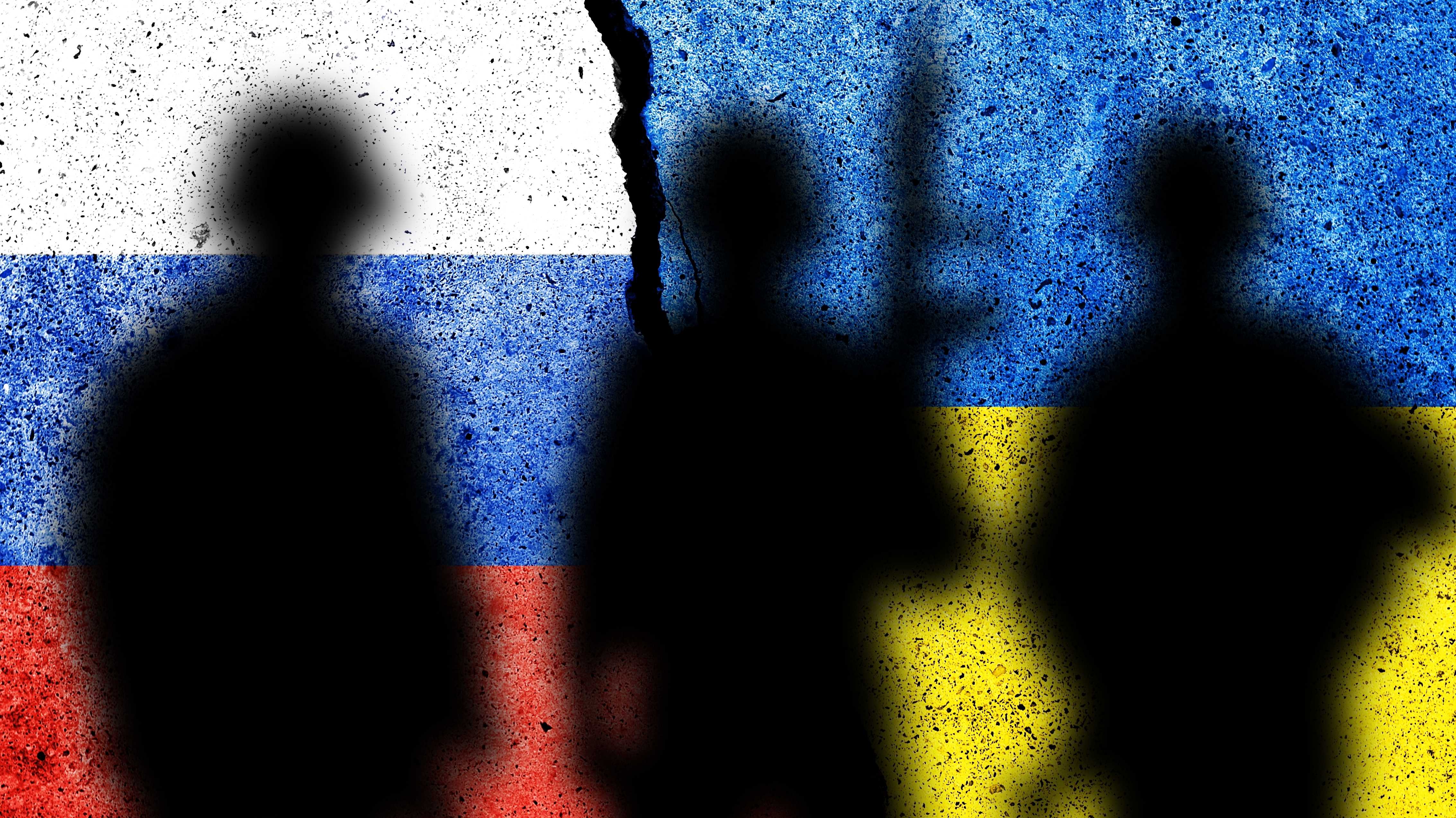 Der Schatten von Soldaten vor dem Hintergrund russischer und ukrainischer Flaggen.