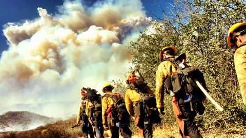 5 Feuerwehrmänner gehen durch brennendes Gelände
