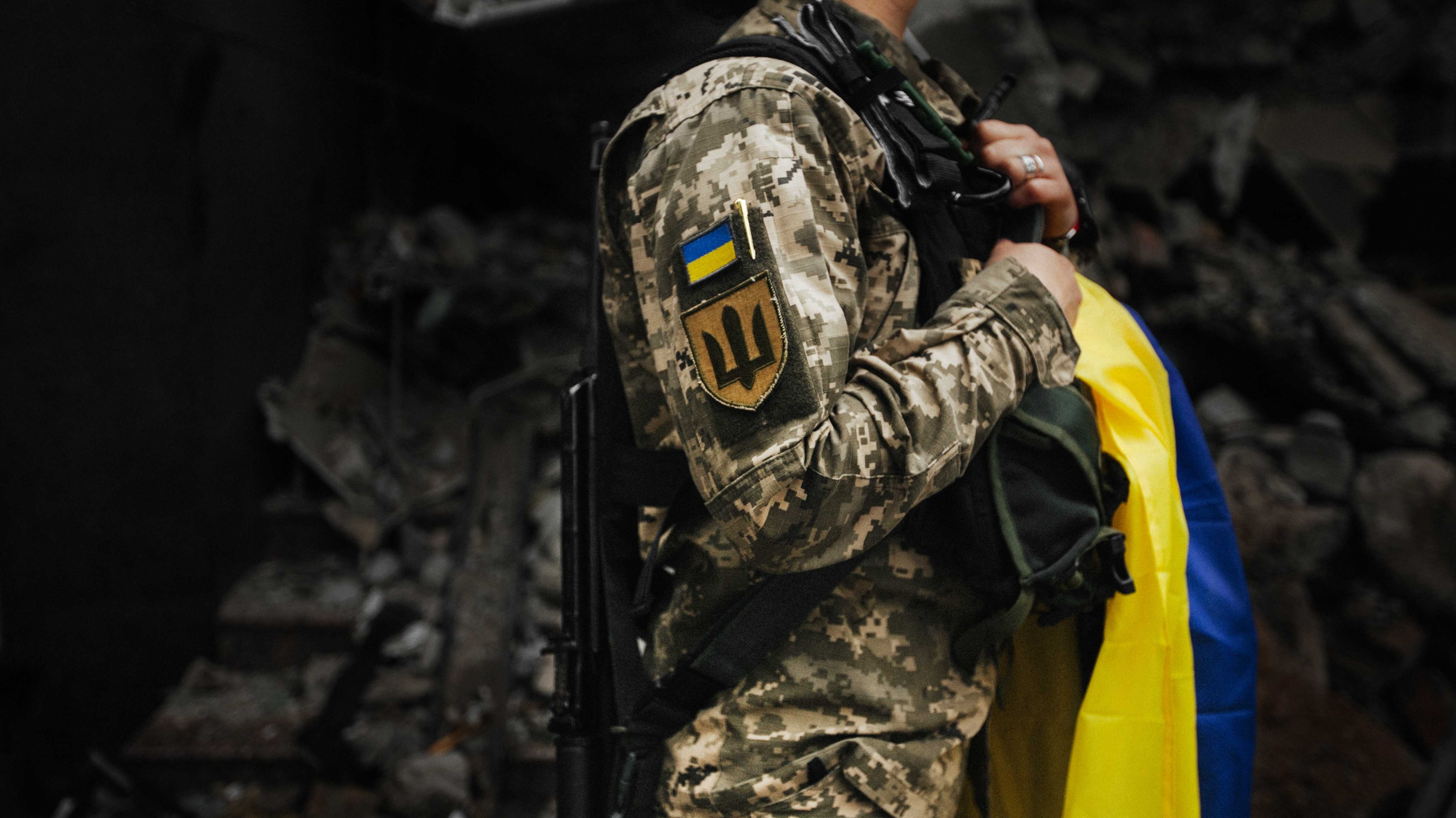 Ukrainische Soldatin mit Flagge vor einem zerstörten Haus.