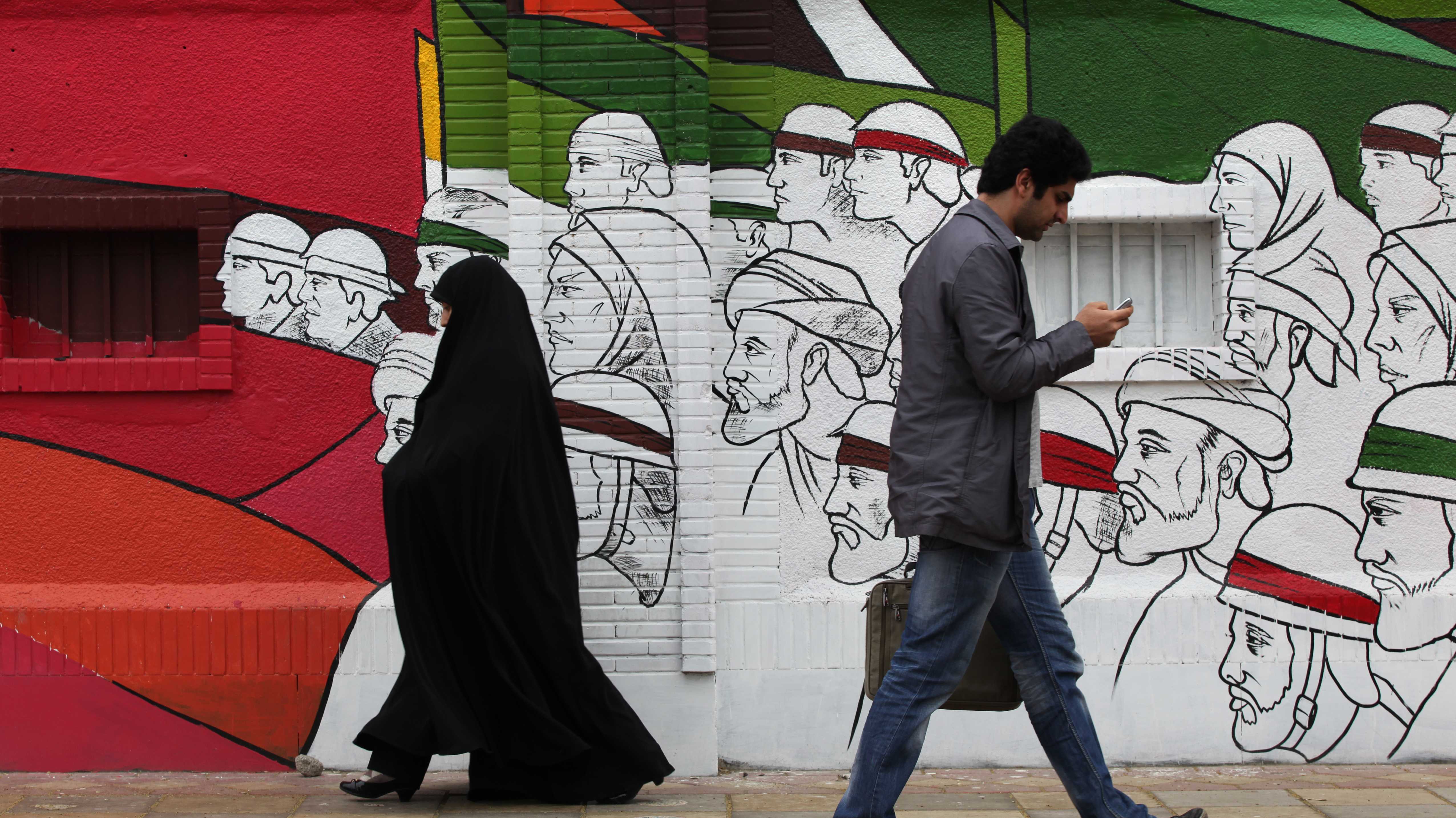Iraner:innen gehen in der Imam Khomeini Straße in Teherans Zentrum, im Hintergrund Graffiti auf einer Hauswand