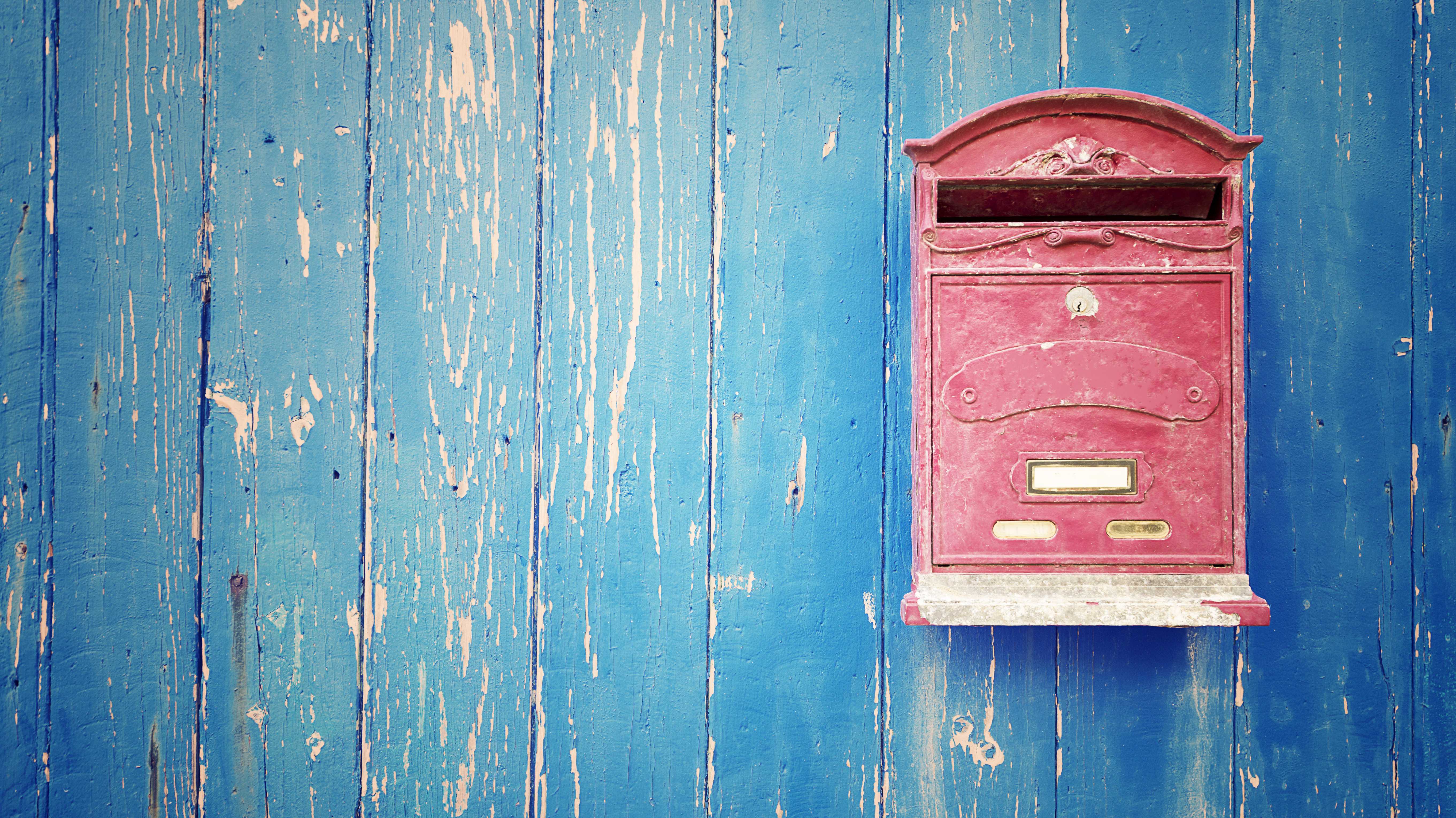 Ein roter Briefkasten an einer blauen Holzwand.