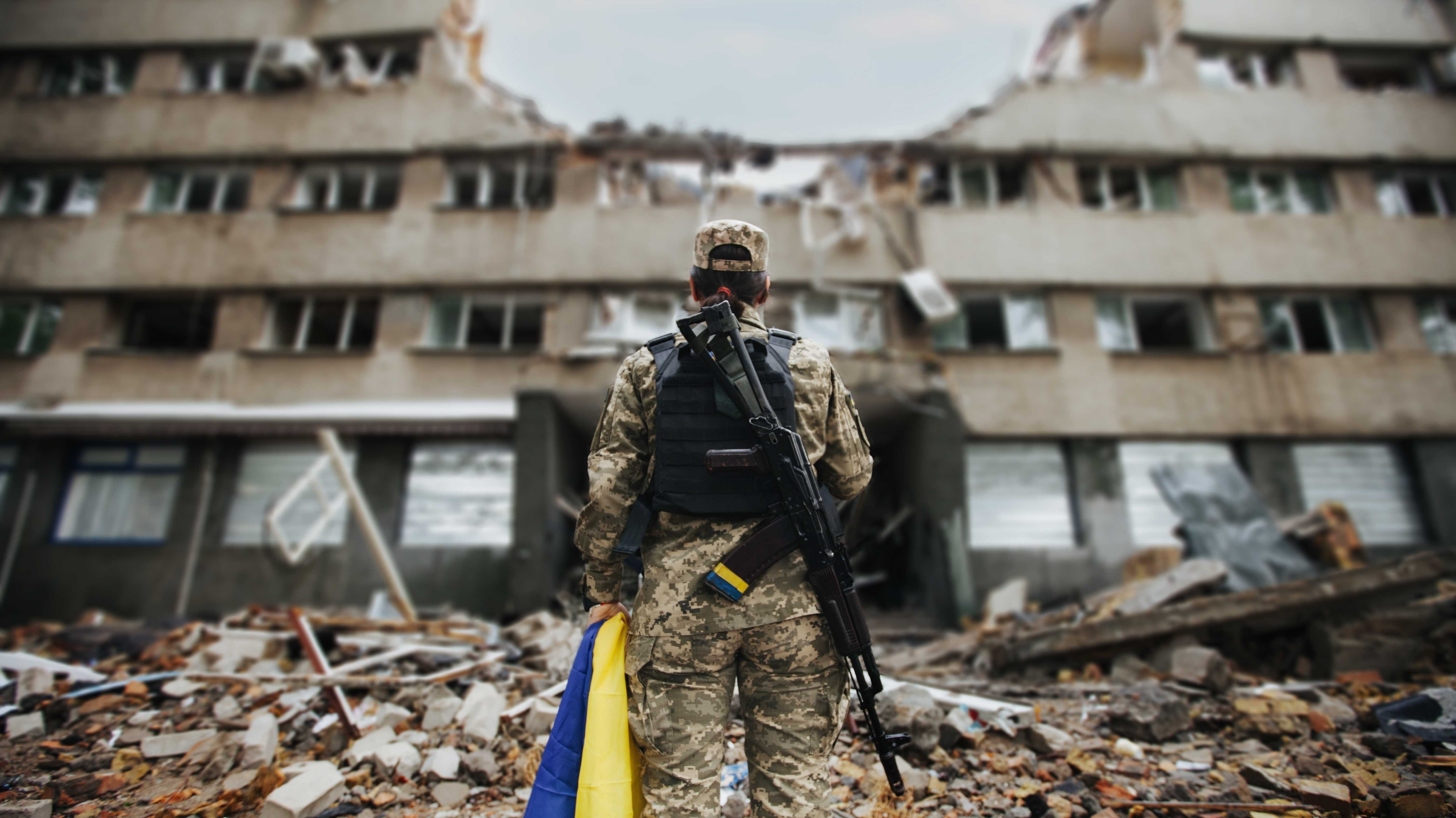 Ukrainische Soldatin mit Flagge vor einem zerstörten Haus
