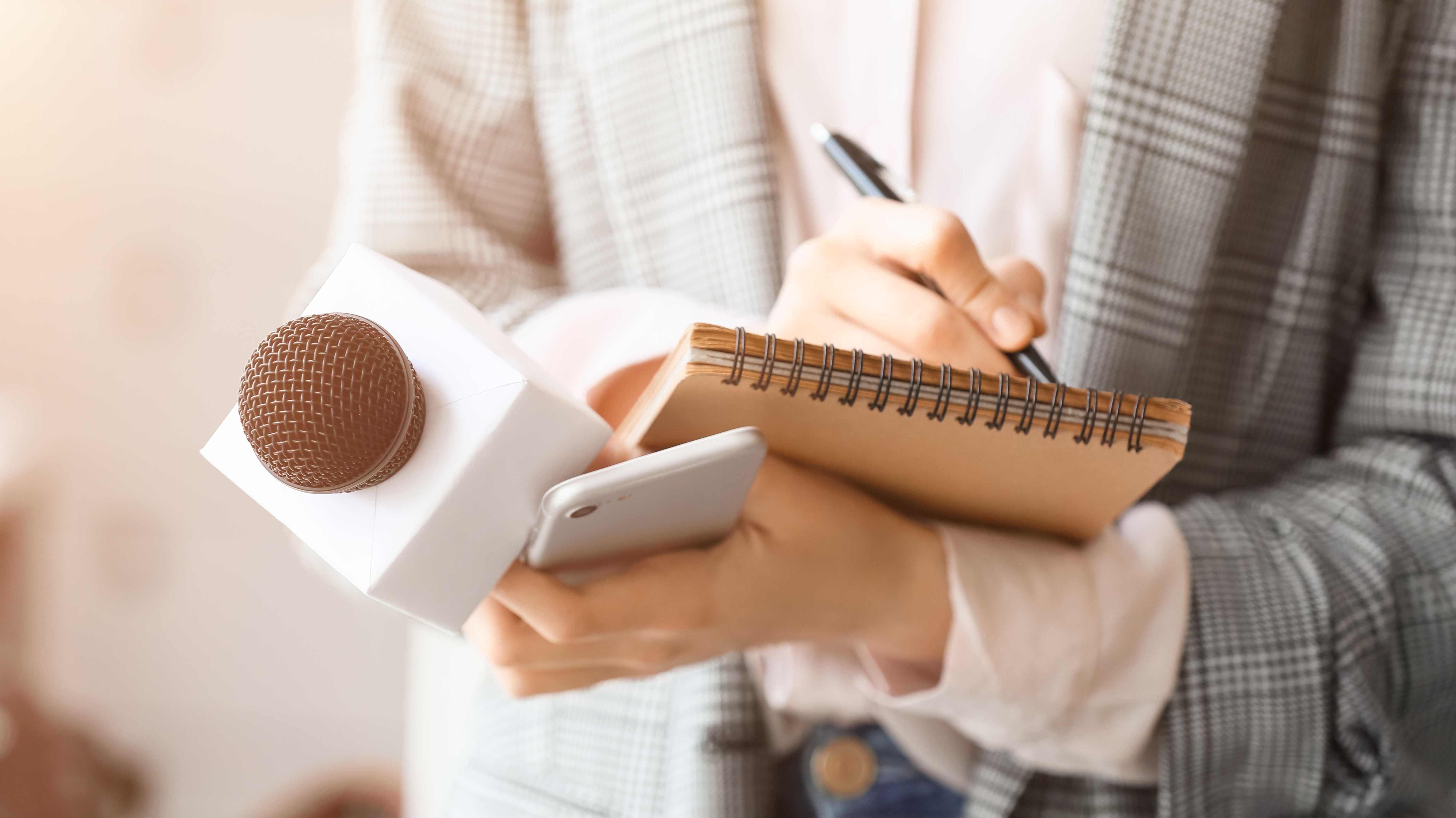 Journalistin mit Mikrofon, Notebook und Telefon im Büro