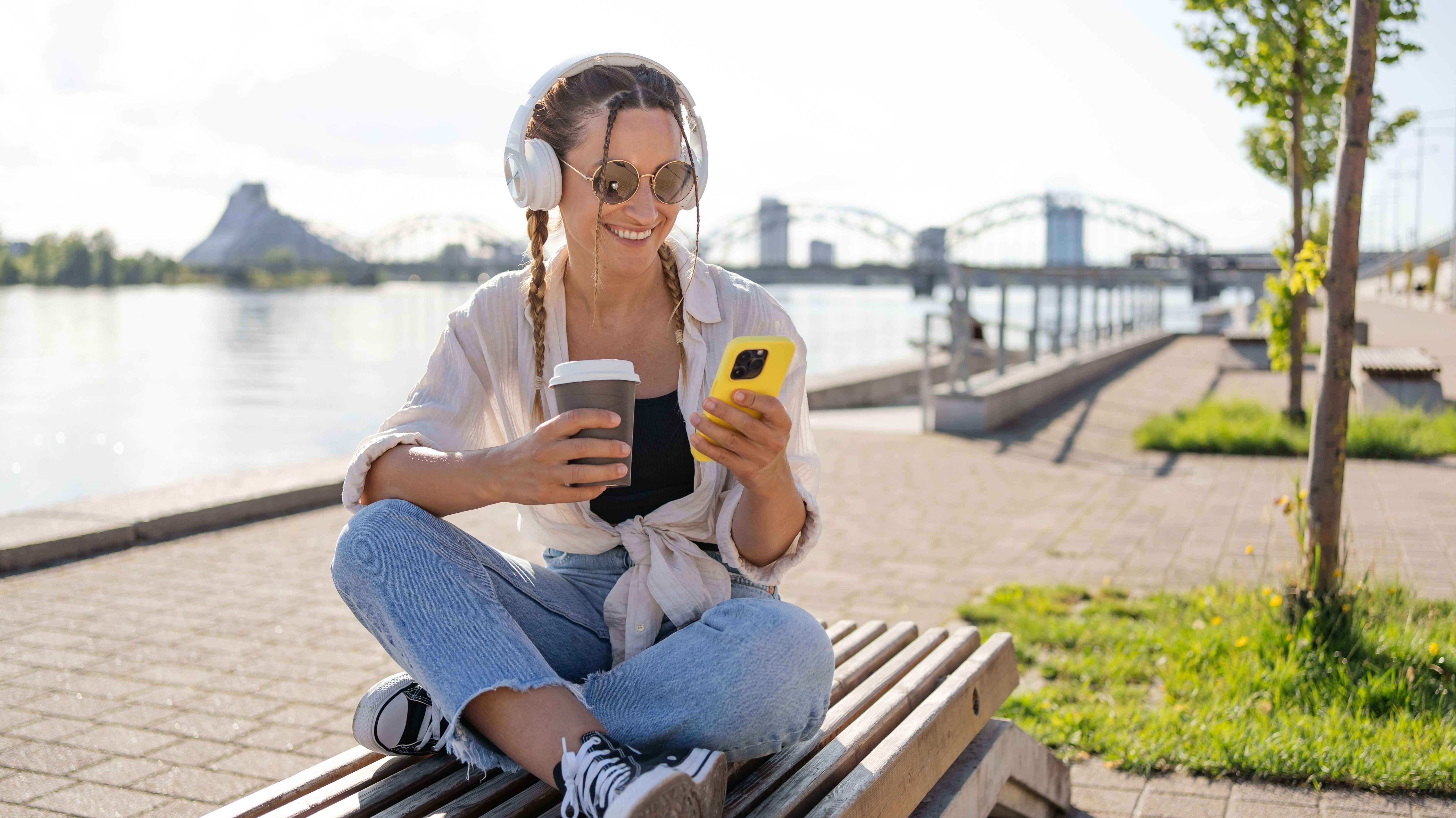 Hipster-Frau in Bluetooth-Kopfhörern genießen positive Musik-Playlist aus dem mobilen Radio mit 4g Wireless in der Stadt.