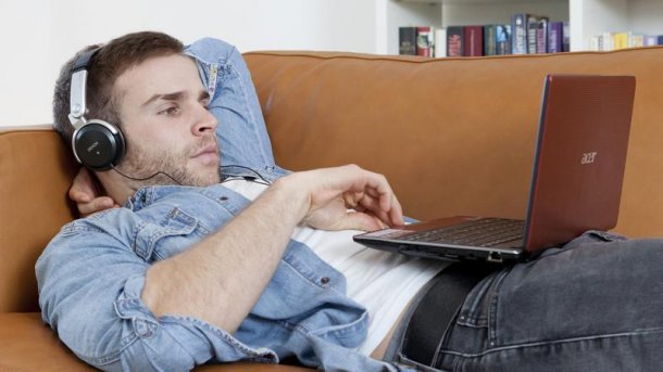 Mann mit Kopfhöhrern und Laptop auf Sofa