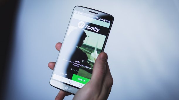 Hand hält Handy mit aktiver Spotify-App