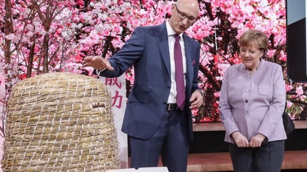 Telekom-Chef Timotheus Höttges zeigt Bundeskanzlerin Angela Merkel, wie er Bienen helfen möchte