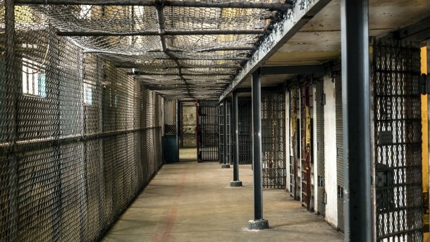 Vergitterter Gang in einem Gefängnis, rechts Zellentüren