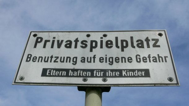 Ein Schild vor blauem Himmel, die Aufschrift lautet: Privatspielplatz - Benutzung auf eigene Gefahr - Eltern haften für ihre Kinder