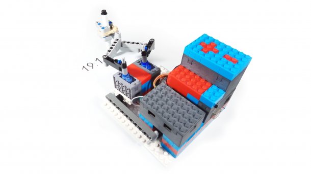 Ein bunter Lego-Aufbau hält mit zwei Ärmchen einen Stift, der die Uhrzeit schreibt