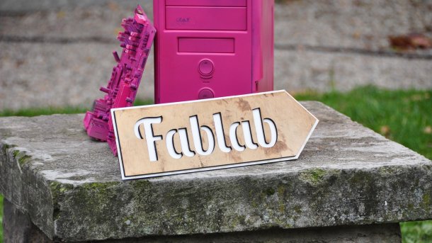 Schild "Fablab" vor einem rosa angesprühten Rechner
