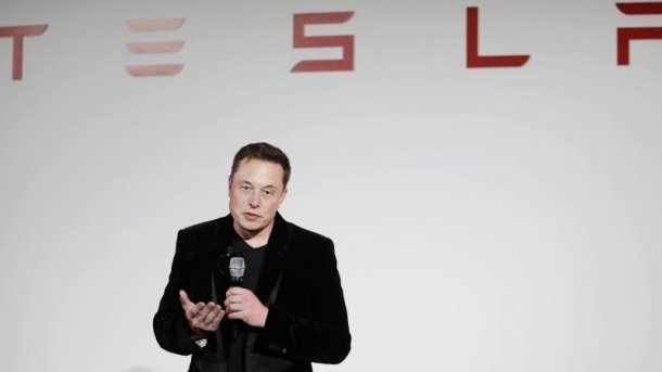 Elon Musk auf Bühne vor Tesla-Schriftzug