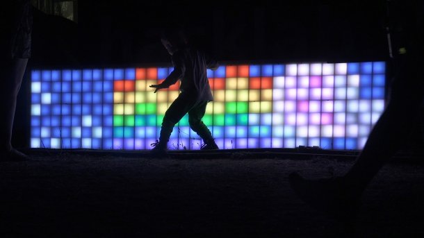 Schatten eines Kindes in der Nacht, vor bunter LED-Wand mit Nyan Cat.